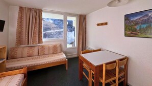 Ein gemütliches Zimmer mit einer Couch, einem Esstisch, einem Fenster mit Vorhängen und einem Bild an der Wand.