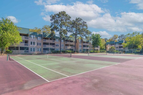 An outdoor tennis court with a net, surrounded by multi-story buildings with balconies.