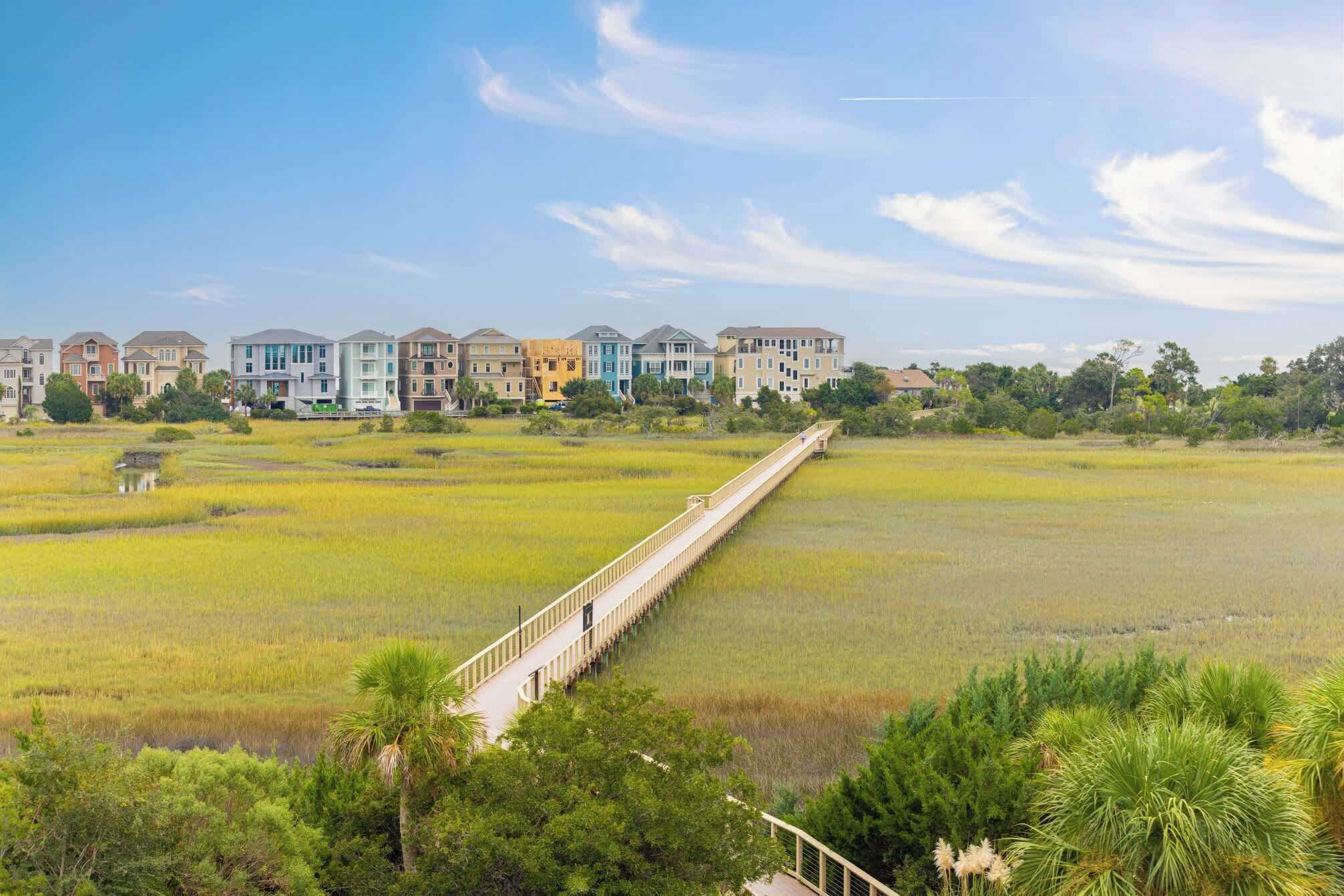 A coastal residential area with a long wooden boardwalk leading to a row of colorful houses.