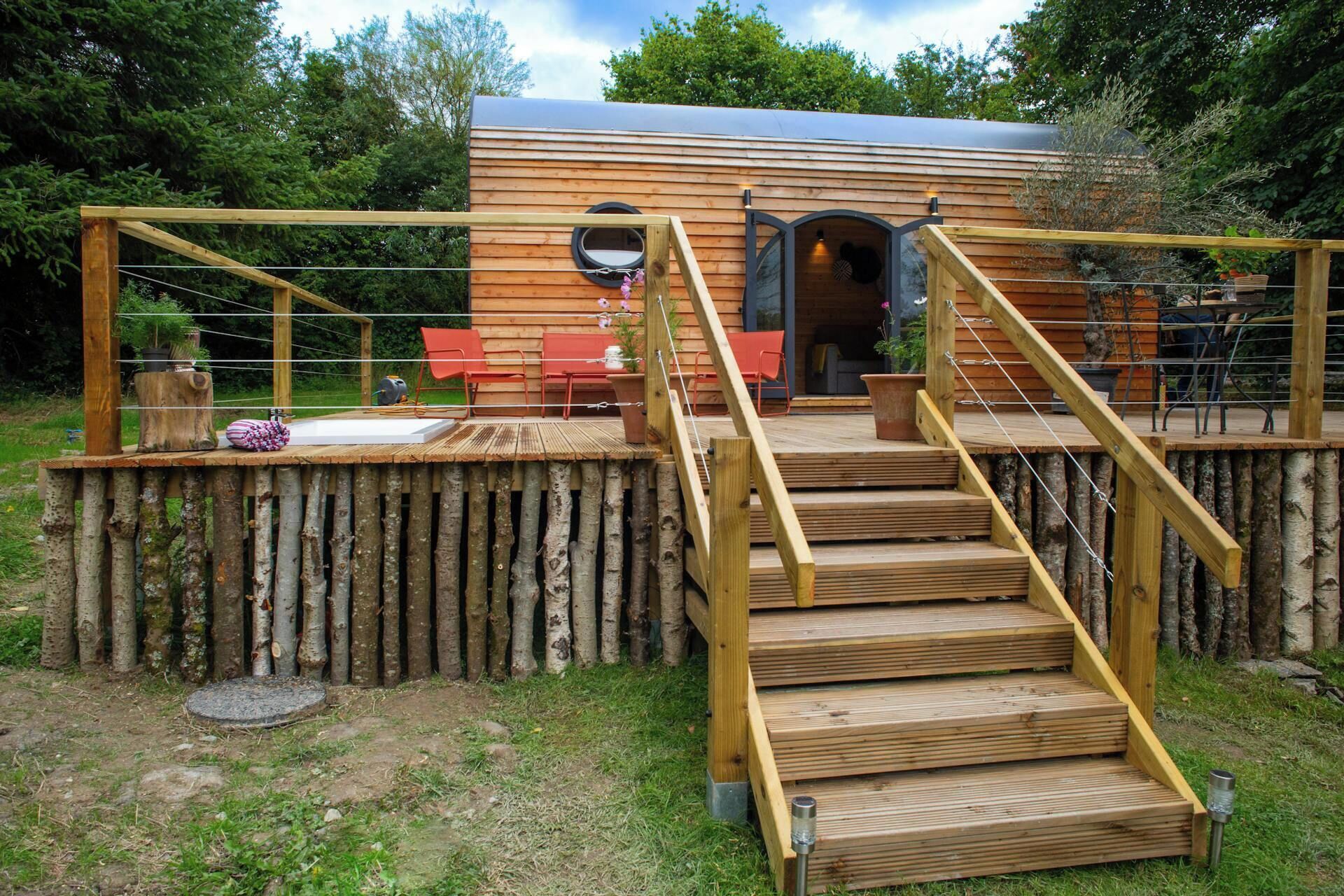 A wooden cabin with a deck, a staircase, and a door leading to an interior space.