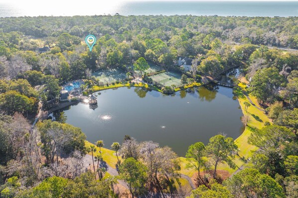 An aerial view of a lake surrounded by dense greenery and a tennis court.