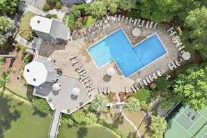 An aerial view of a property with a swimming pool, lounge chairs, and a tennis court.