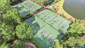 Vista aérea de un complejo de canchas de tenis rodeado de árboles y una masa de agua.
