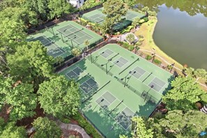 Ein weiter Blick von oben auf einen Tennisplatzkomplex, umgeben von Bäumen und einem Gewässer.