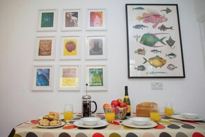 A breakfast table with various food items and drinks, a coffee pot, and a large fish illustration on the wall.
