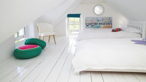 An attic bedroom with a bed, a chair, two bean bags, a window, and a painting.