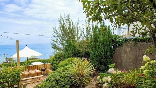 A garden with a wooden deck, a barbecue grill, and a white umbrella.