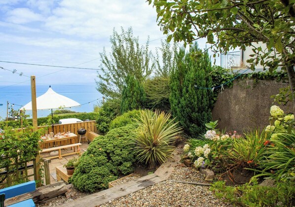A garden with a wooden deck, a barbecue grill, and a white umbrella.