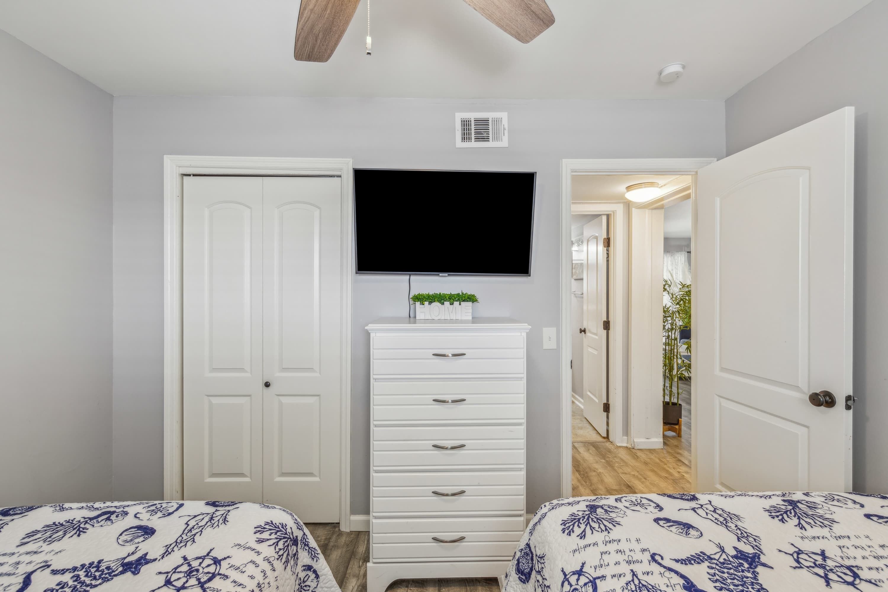 A bedroom with two beds, a dresser, a TV, and a ceiling fan.