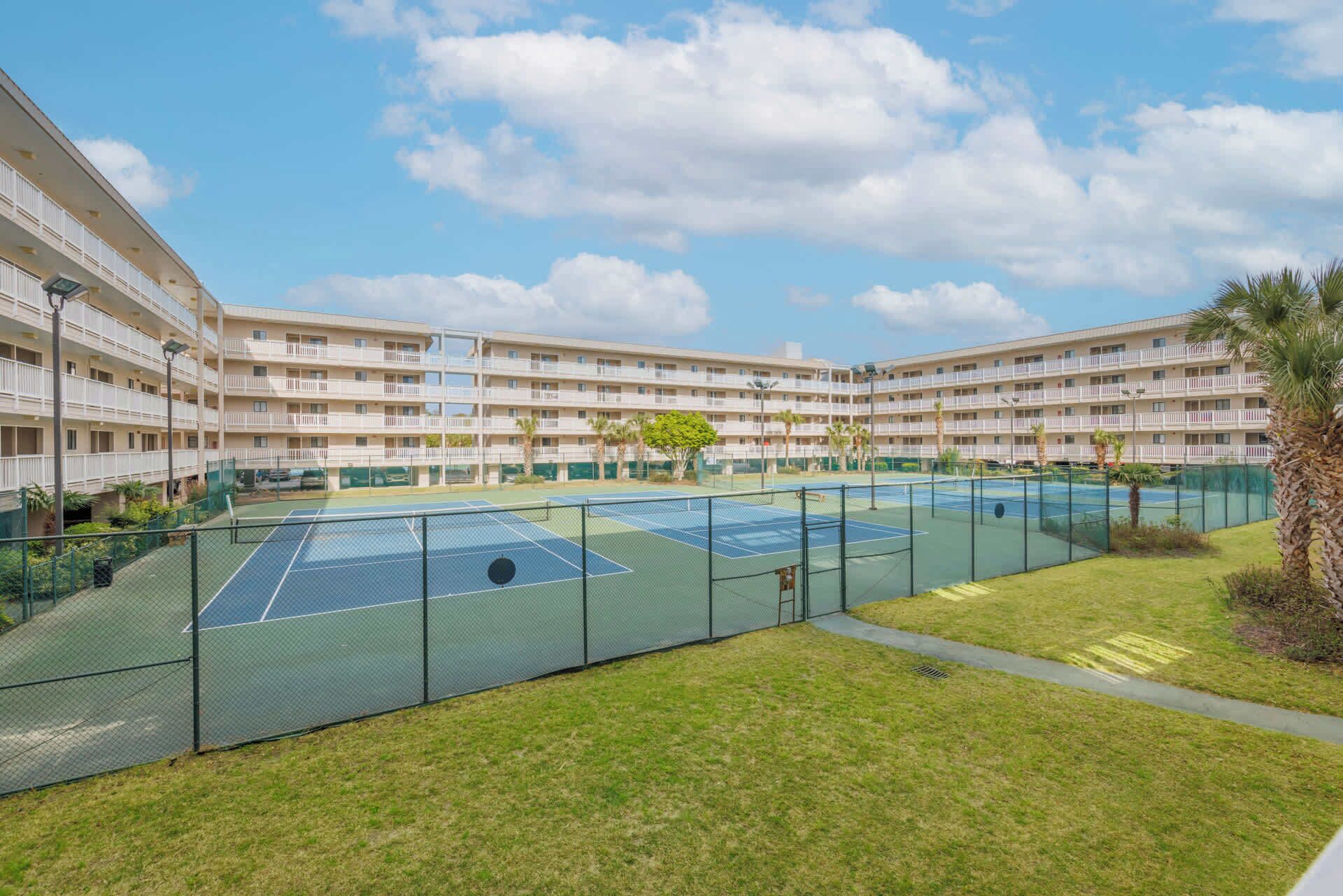 Un hotel de varios pisos con cancha de tenis y zonas verdes a su alrededor.