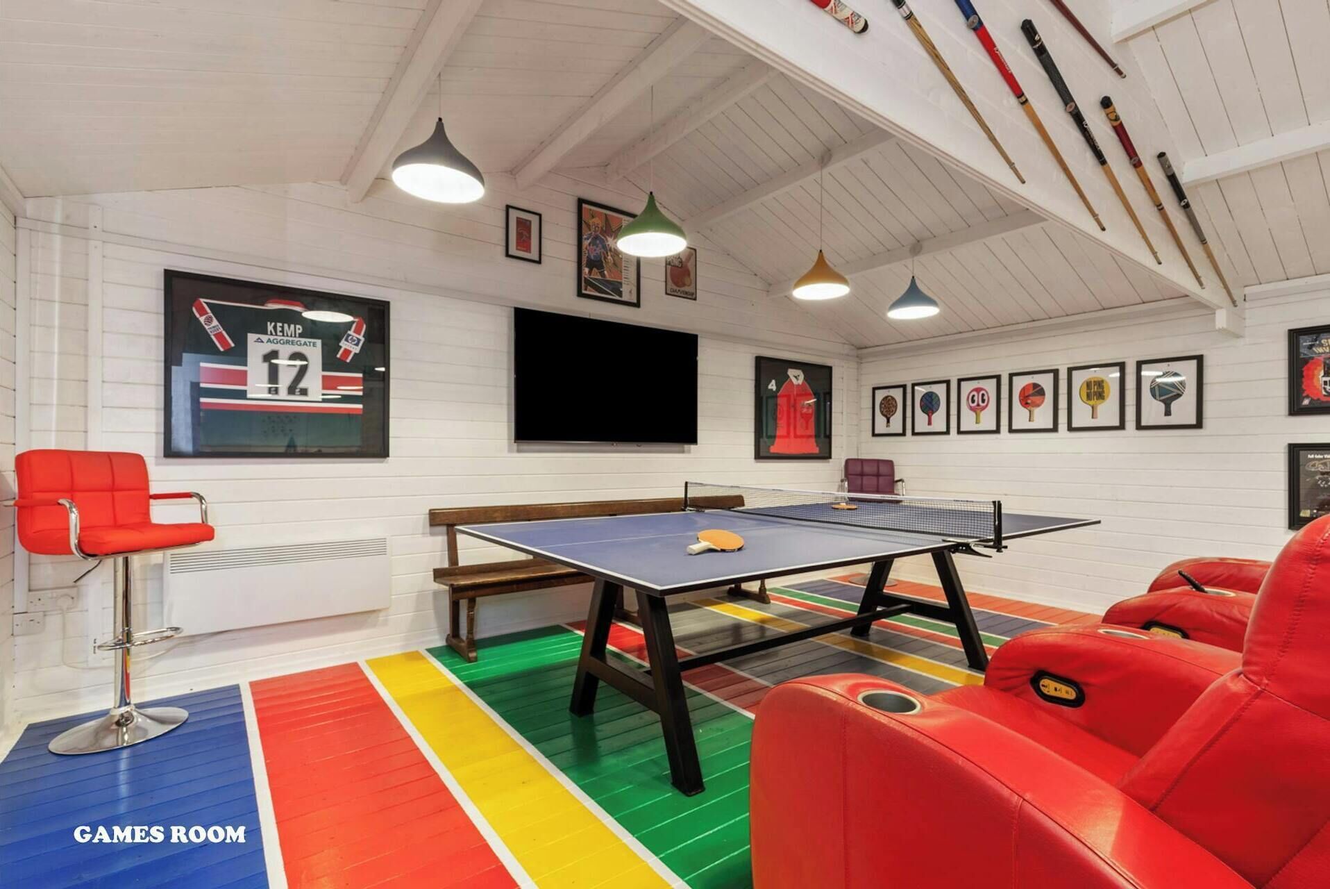 A games room with a ping pong table, red seating, and sports memorabilia on the walls.