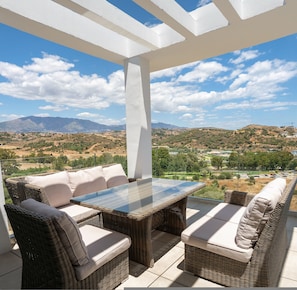 A covered outdoor seating area with wicker furniture and a glass table, overlooking a mountainous landscape. - Overlook Apartment in Mijas - Ref 254 (Mijas)