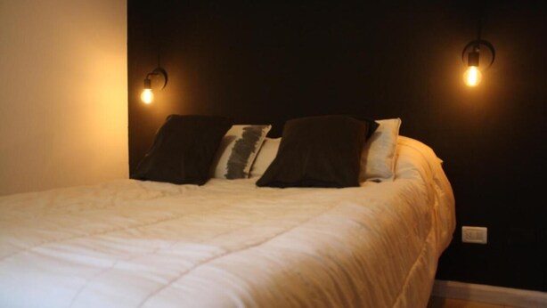 A bed with a white duvet, two wall-mounted lights, and a dark wall. - Charming 1-bedroom apartment with WiFi, AC in fabulous GFJ (GFJ)