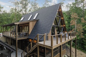 A modern, wooden cabin with a sloped roof, multiple decks, and outdoor seating areas. - Luxury A-Frame: Pets, Pickleball & Peloton w/Views (Mineral Bluff)