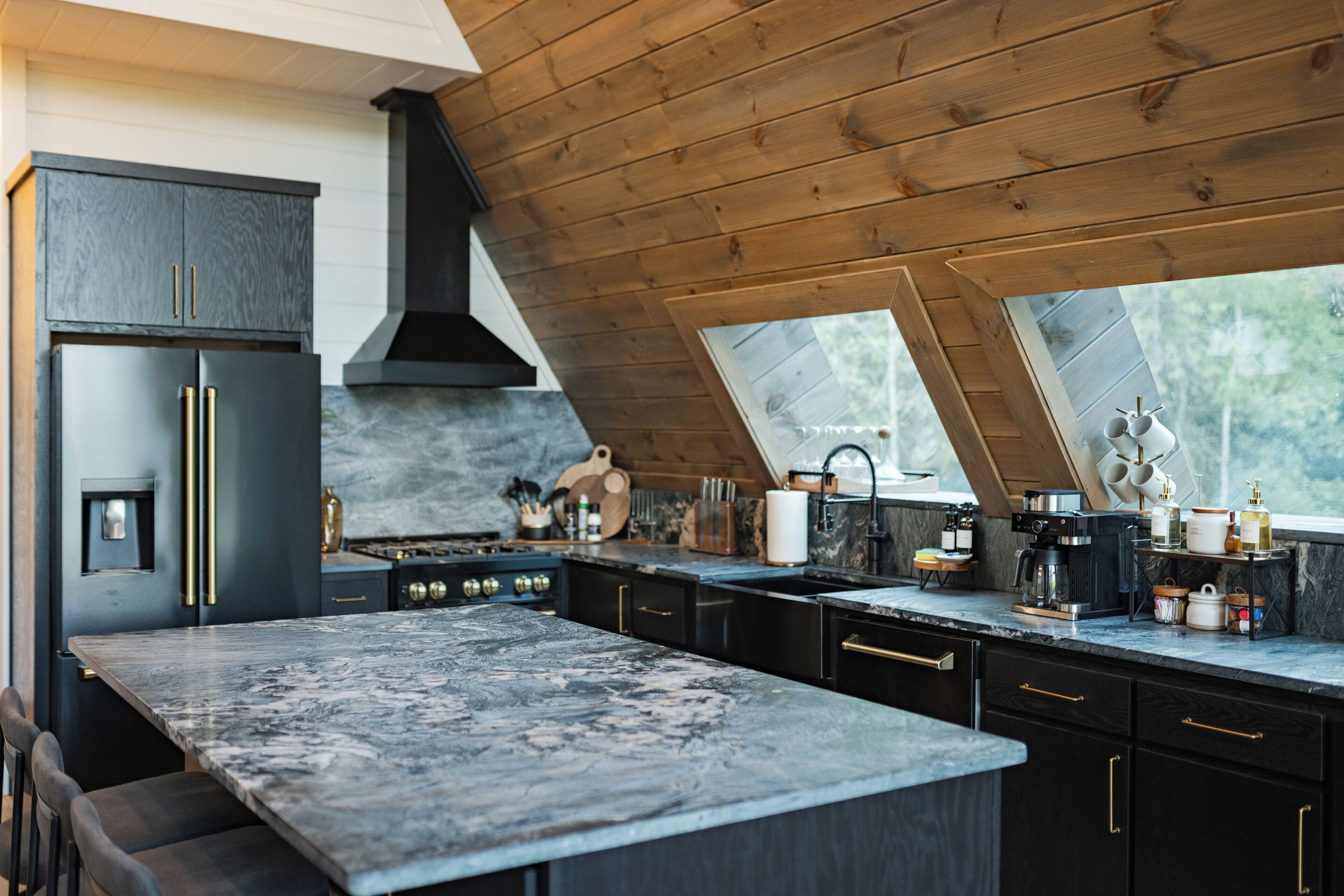 A modern kitchen with dark cabinetry, a large marble island, and a skylight.