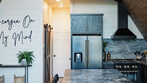 A modern kitchen with a large island, wooden ceiling beams, and a built-in stove. - Luxury A-Frame: Pets, Pickleball & Peloton w/Views (Mineral Bluff)