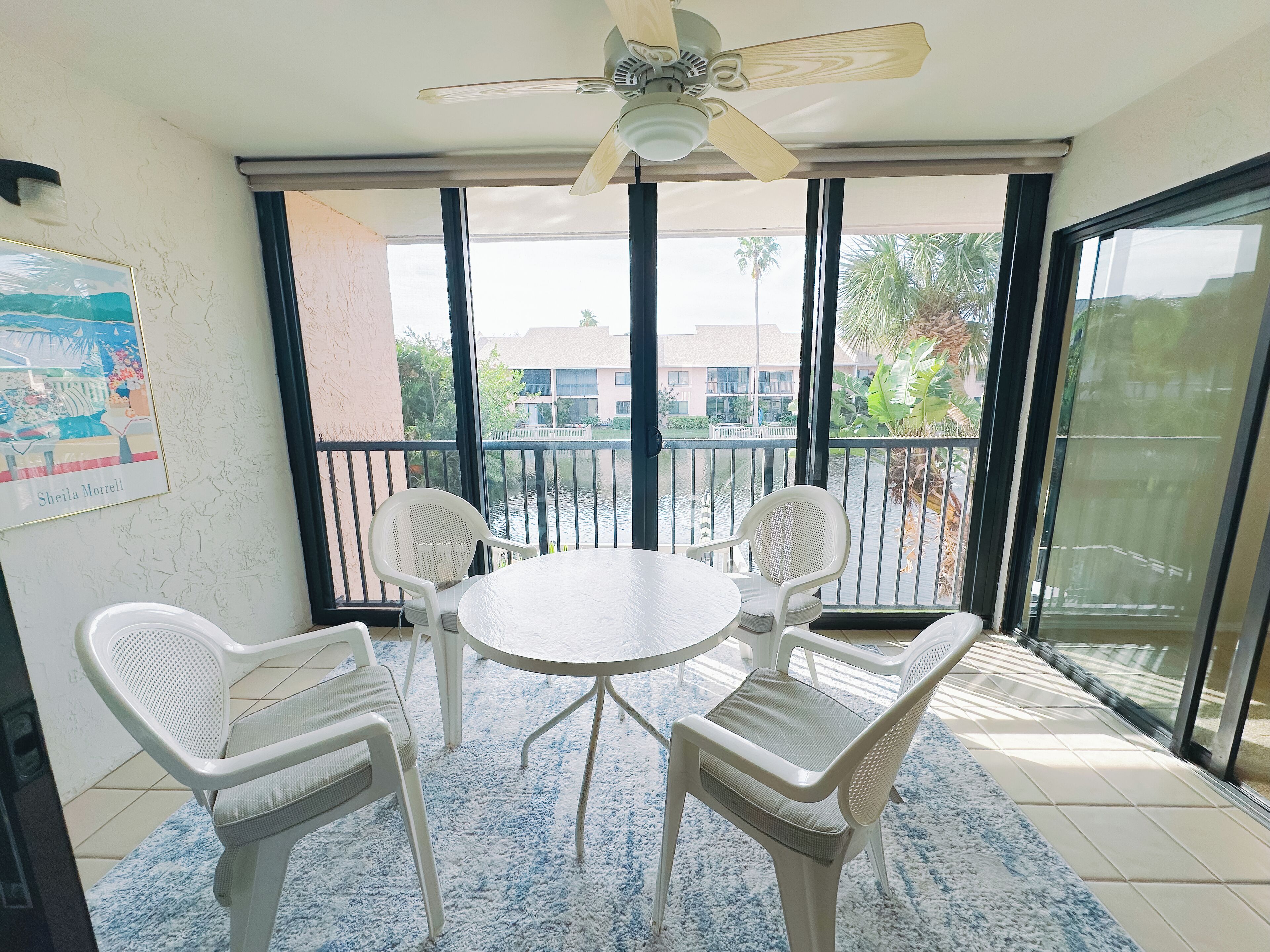 Ein Balkon mit rundem Tisch, vier Stühlen, großen Fenstern und einem Deckenventilator.