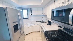 Una cuina moderna amb armaris blancs, un frigorífic d'acer inoxidable, un microones i una placa de cocció.