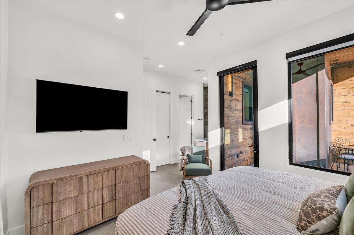 Un dormitorio moderno con una cama grande, un televisor montado en la pared, un armario de madera y un ventanal corredero que da a un balcón.