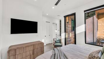 Un dormitorio moderno con una cama grande, un televisor montado en la pared, un armario de madera y un ventanal corredero que da a un balcón.