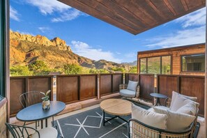 Enjoy breathtaking views of the surrounding mountains from this balcony with a round table, two chairs, and a cozy seating area.