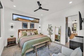 Relax in this serene bedroom with a large bed, bench, and ceiling fan. Enjoy a view of the outdoors from the large window.