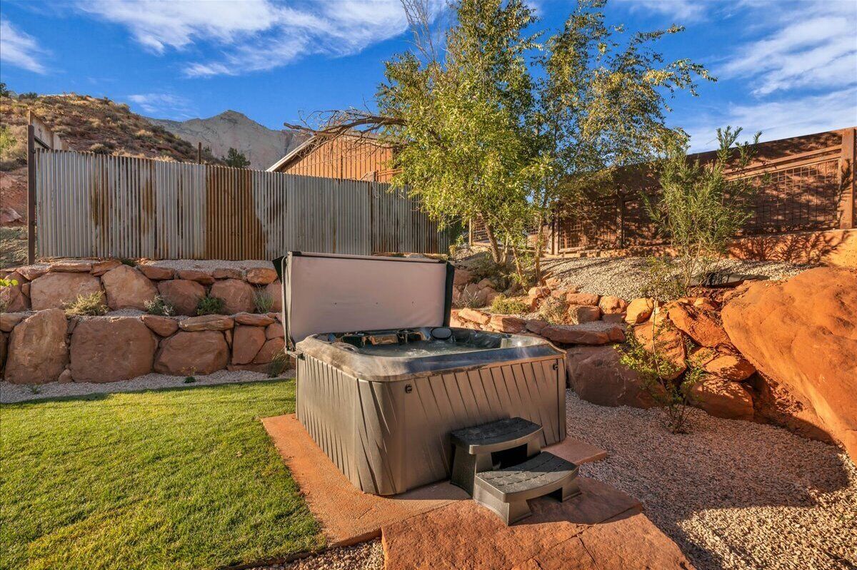 A hot tub in a landscaped outdoor area with a stone wall, a wooden fence, and a tree.