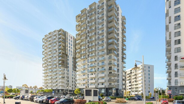 A high-rise residential building with multiple balconies, a parking area, and a clear sky. - Albatross Tower by Grand Apartments (Gdansk)