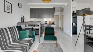 A modern living room with a striped sofa, a green armchair, and a dining area with a lamp and a shelf. - Albatross Tower by Grand Apartments (Gdansk)