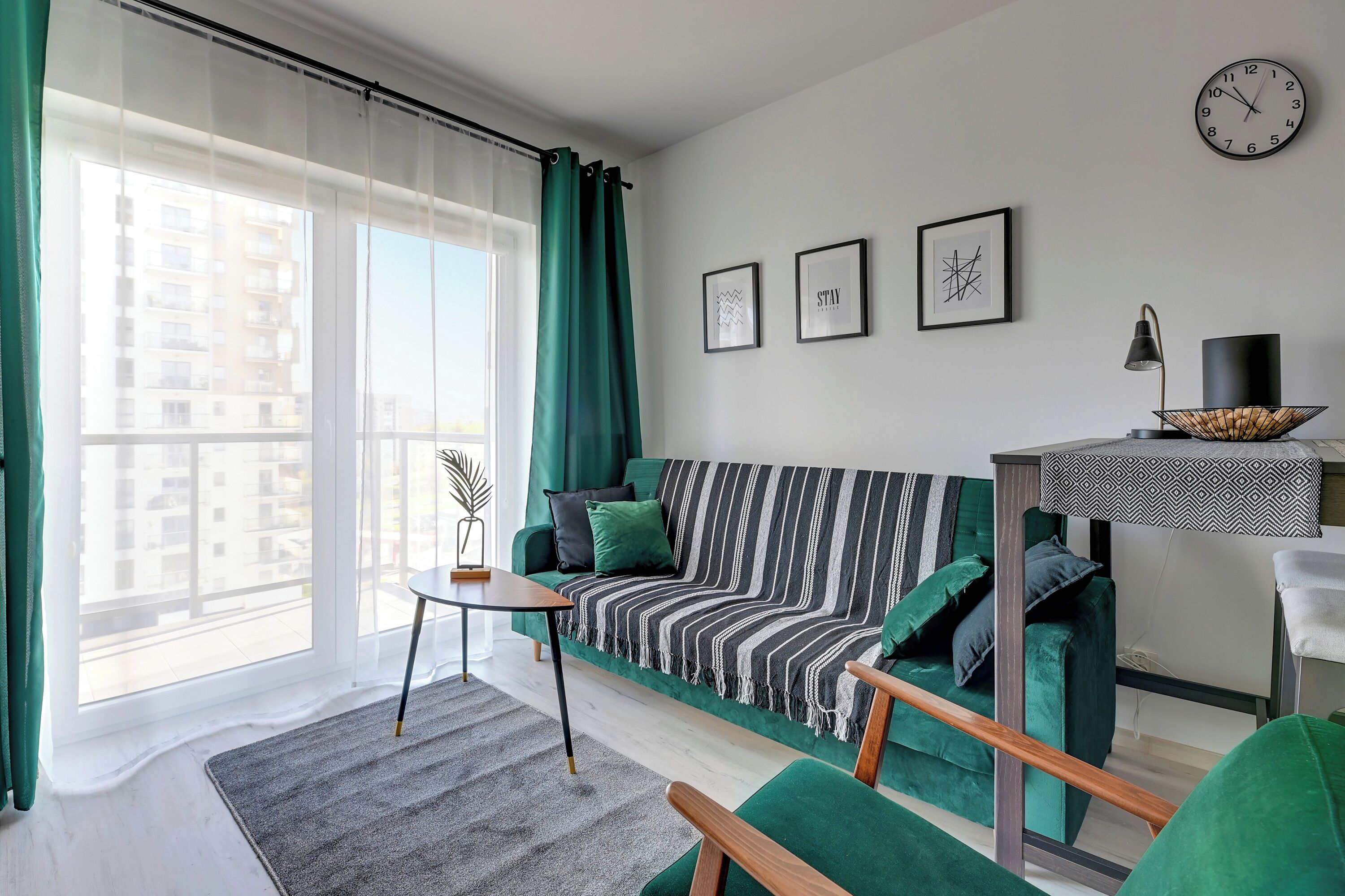 Ein modernes Wohnzimmer mit einem grünen Sofa, einem kleinen Tisch und Blick auf die Stadt durch große Fenster.
