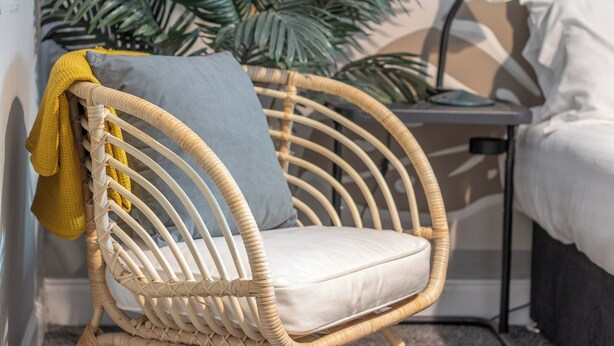 Une chaise en osier avec un coussin, une serviette jaune et un oreiller gris.