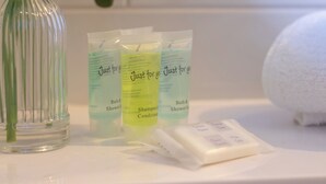 Un meuble-lavabo de salle de bain avec un flacon en verre transparent, trois échantillons de shampoing et un savon.