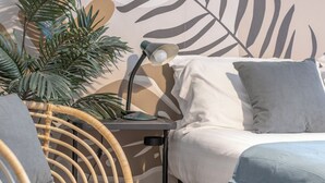 Une chambre à coucher avec un lit, une table de chevet, une lampe, une plante en pot et une chaise en osier.