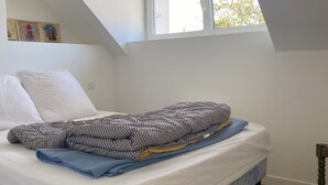 Un dormitorio con techo inclinado, una cama con manta estampada, una ventana y suelo de madera.