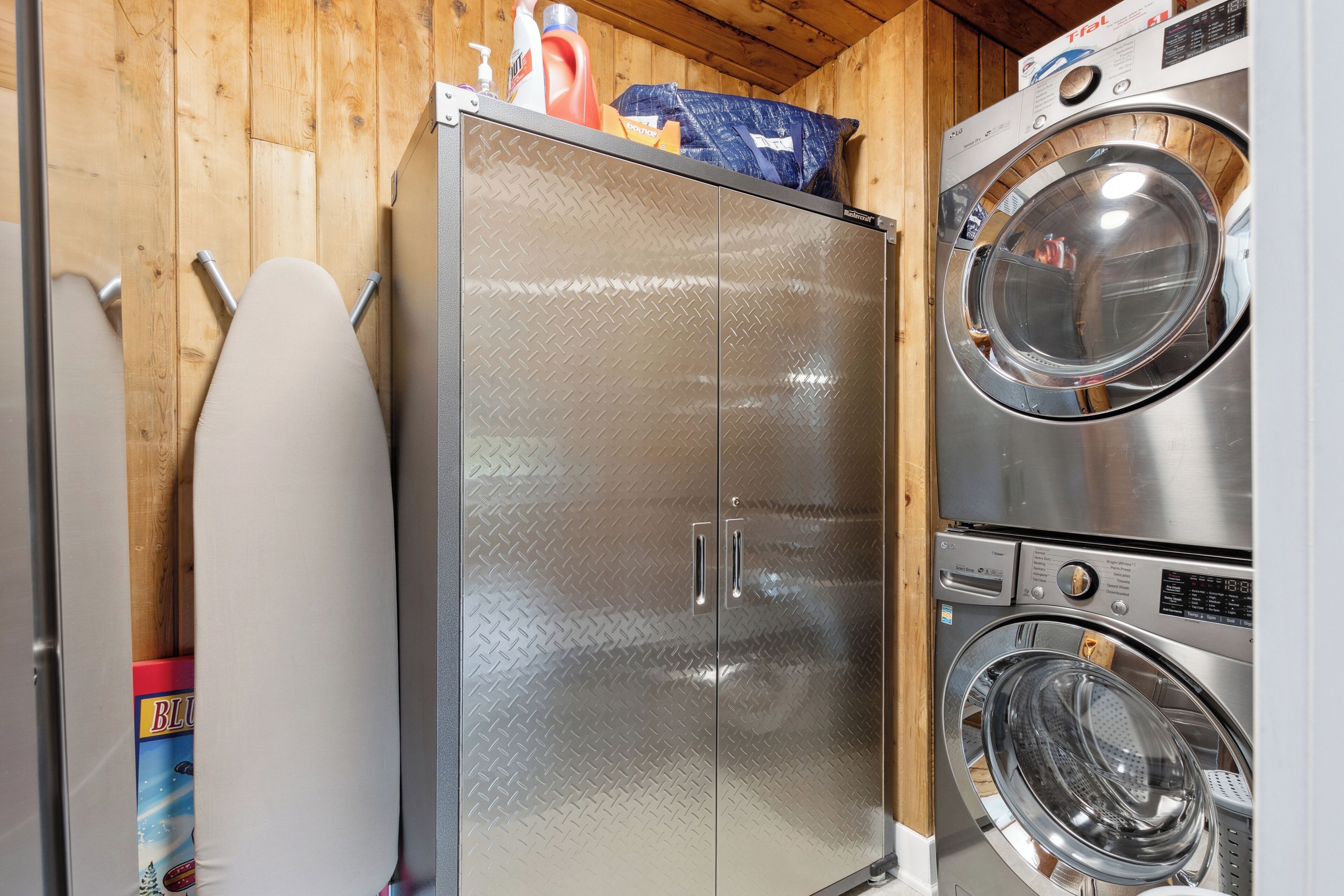Une petite buanderie équipée d’un lave-linge et d’un sèche-linge en acier inoxydable, d’une planche à repasser et d’un meuble dont la surface est recouverte d’une plaque à motifs losangés.
