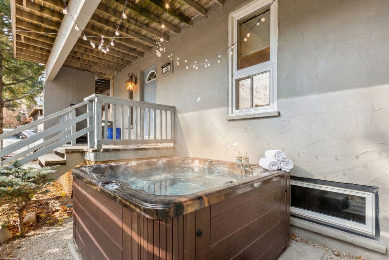 A hot tub outside a house with a wooden deck and stairs leading up to the entrance.