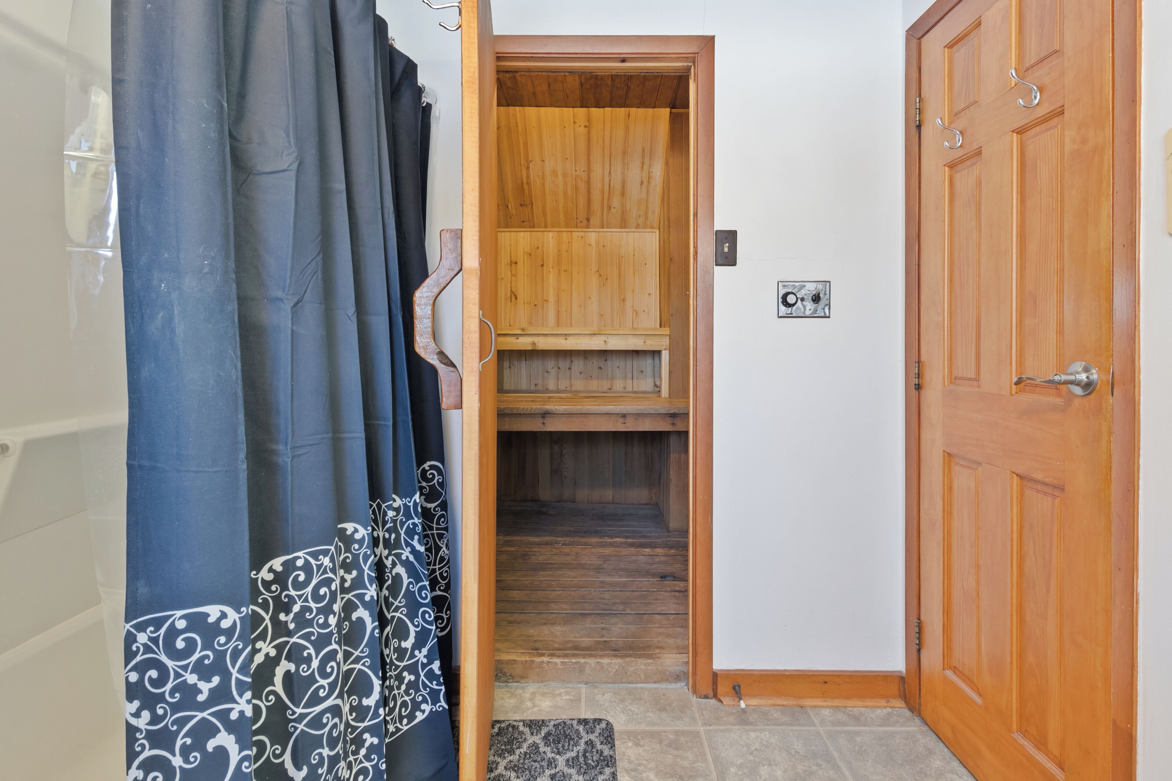 A wooden sauna room with a bench, a wooden door, and a tiled floor.