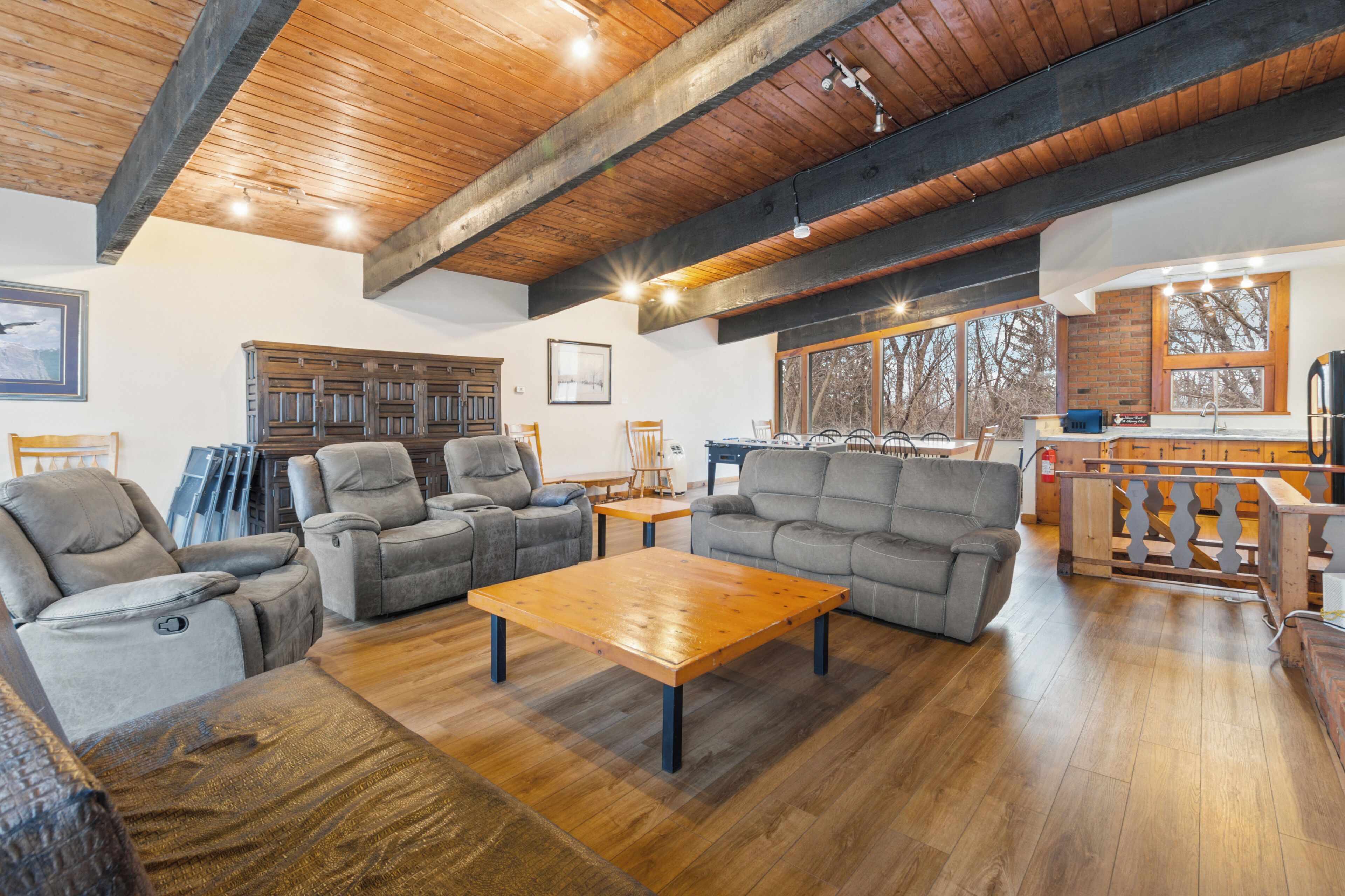 Un salón amplio con techo de madera, sofás grises, una mesa de centro de madera y vistas al exterior a través de grandes ventanales.