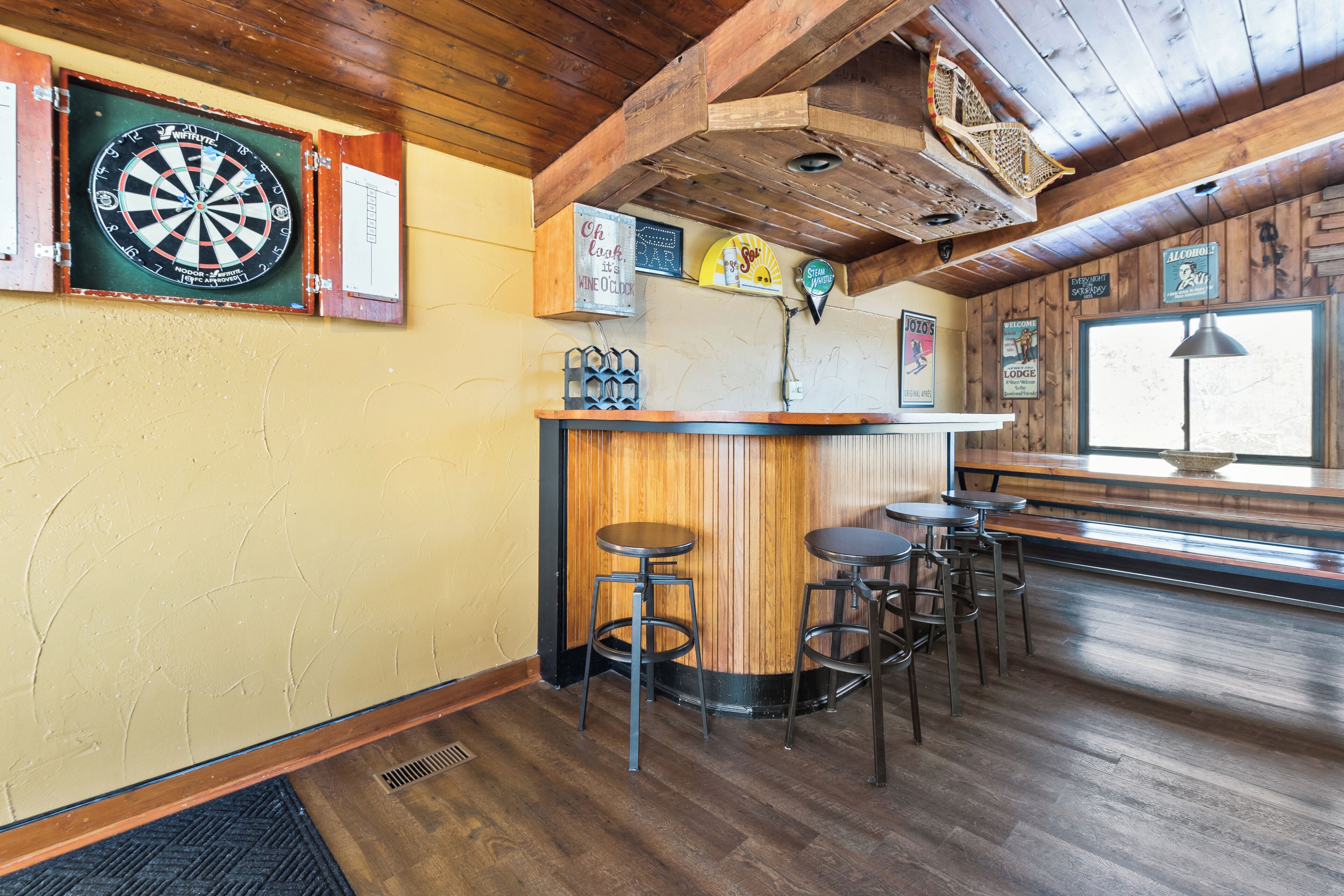 Zona de bar con paredes de madera, un dardo y una barra con taburetes.