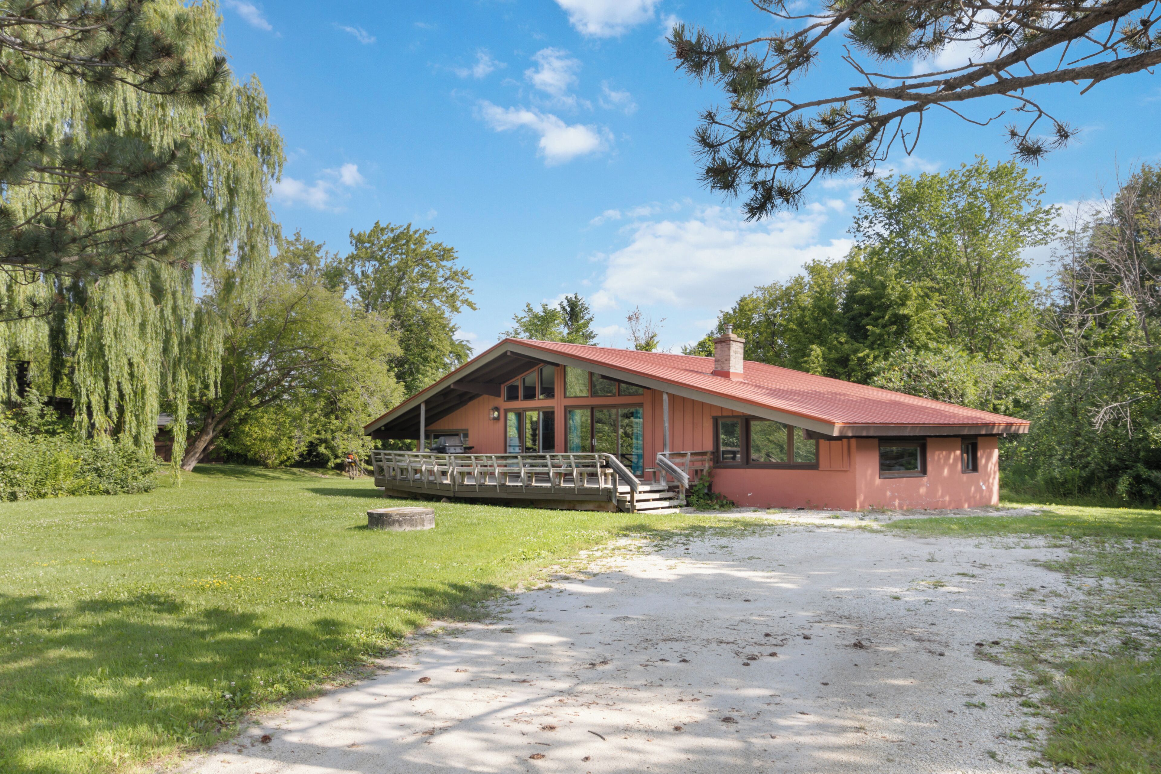 A single-story house with a red roof, a covered porch, and a gravel driveway.