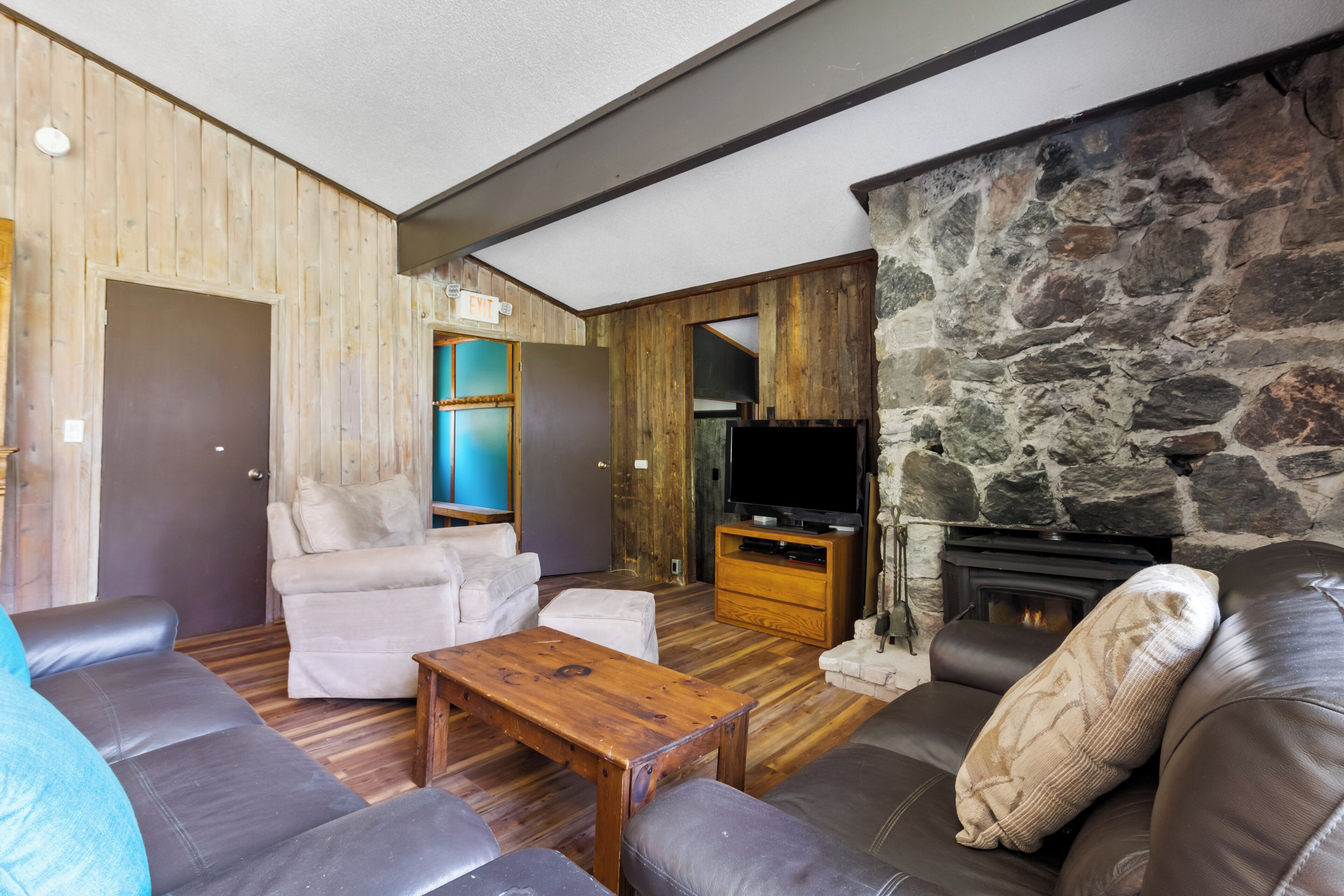 Una sala de estar con chimenea de piedra, sofás de cuero, una mesa de centro de madera y un televisor.