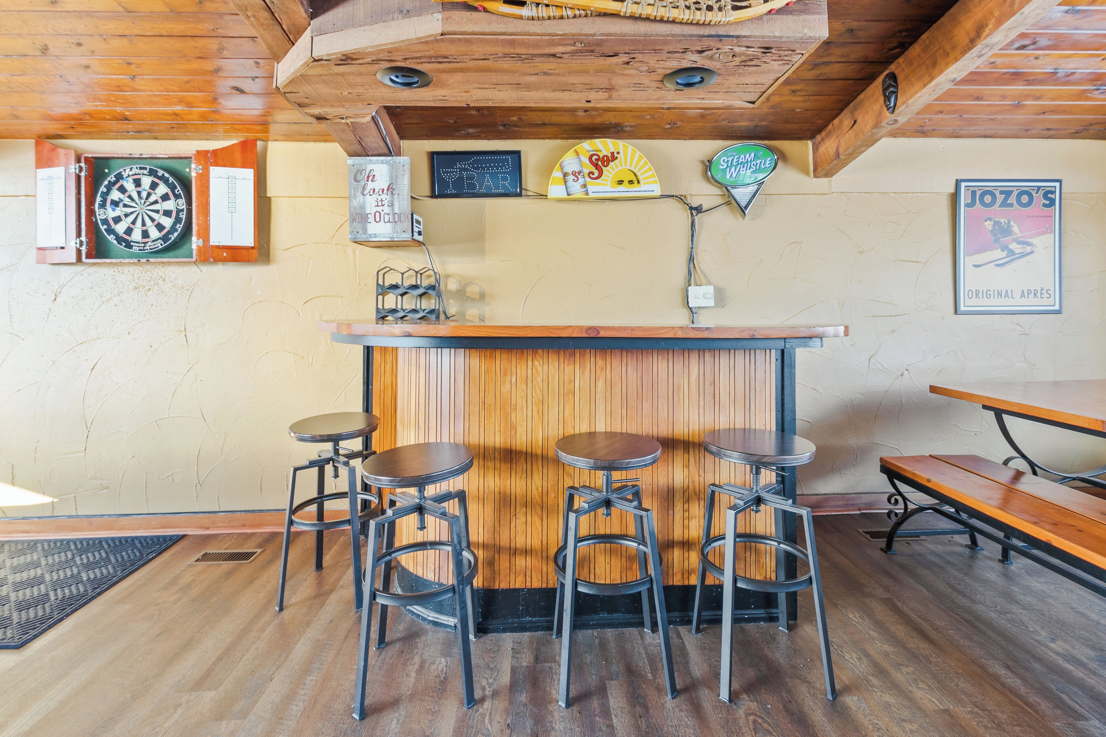 A bar area with wooden ceiling, a dartboard, stools, and a poster on the wall.