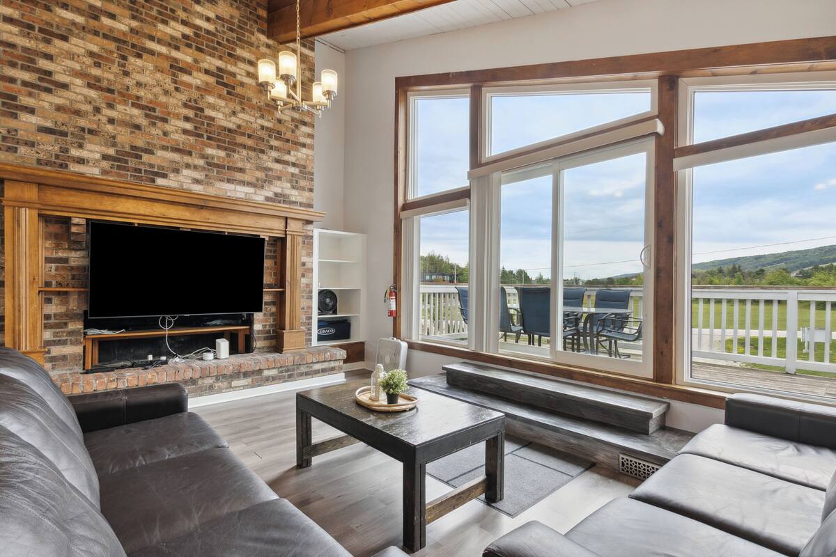 Una sala de estar con chimenea de ladrillo, televisor de pantalla plana y un ventanal con vistas a una terraza.