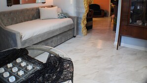 Ein Wohnzimmer mit einer Couch, einem Glastisch mit Spitzenüberwurf und einer Vitrine mit Glastüren.