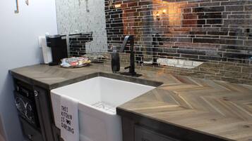 A kitchen with a white sink, dark countertops, and a brick backsplash.