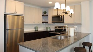 Una cocina moderna con electrodomésticos de acero inoxidable, gabinetes blancos, encimera de granito e iluminación colgante.