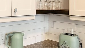 Una cocina con armarios blancos, una planta en un estante, una tetera y un tostador.