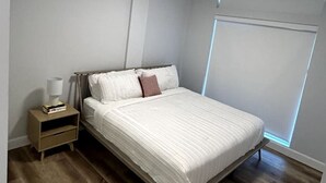 Un dormitorio con cama, mesita de noche, lámpara y ventana con persianas.