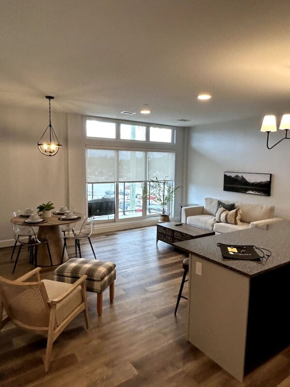 A modern living room with a large window, a dining area with a round table, and a sofa.