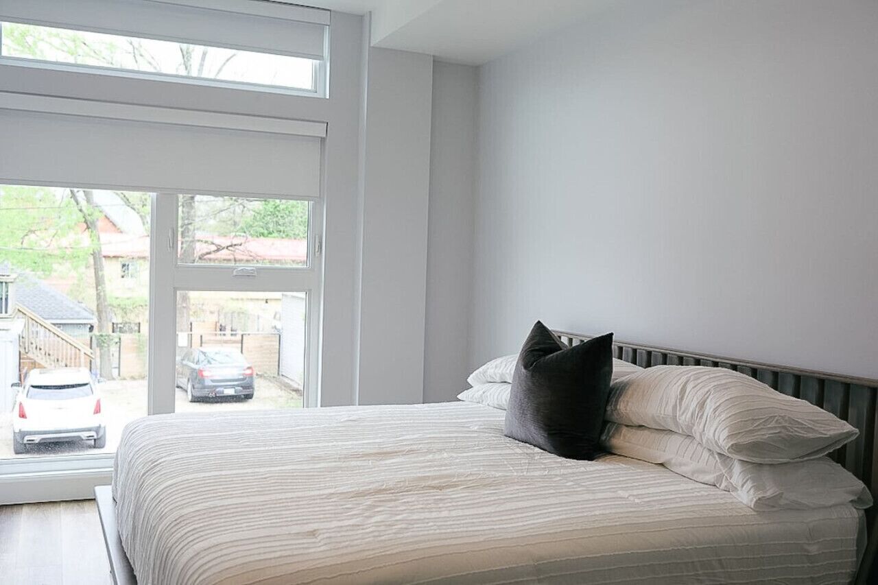 Un dormitorio con un ventanal grande, una cama con ropa blanca y vistas al exterior.